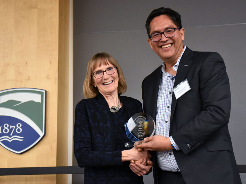 joyce judy and alex hernandez shake hands on stage while holding joyce's award