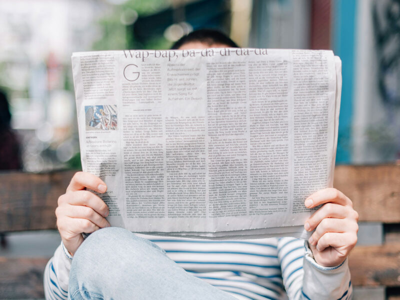 person sits on bench reading newspaper