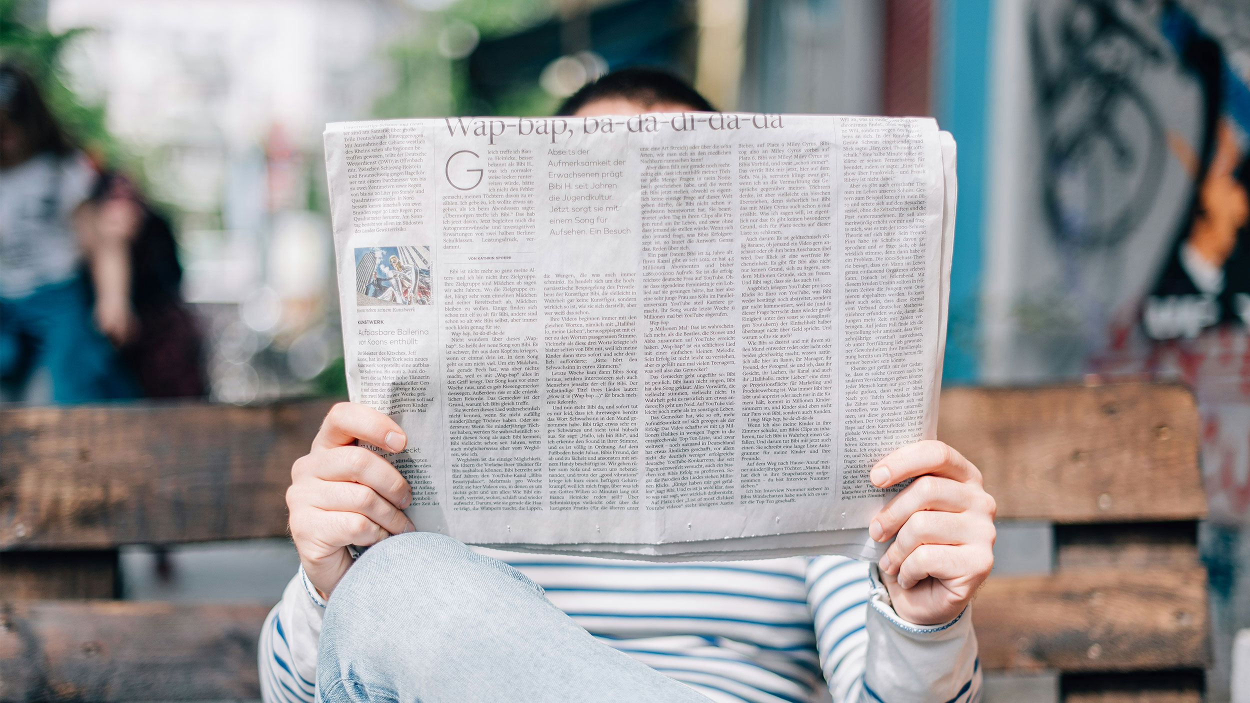 person sits on bench reading newspaper