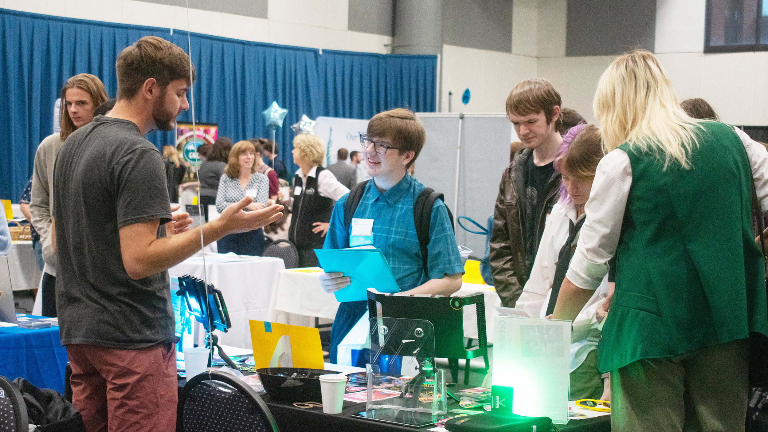 Students look at an employer's table display at the Career Fair and listen closely to the employer speaking