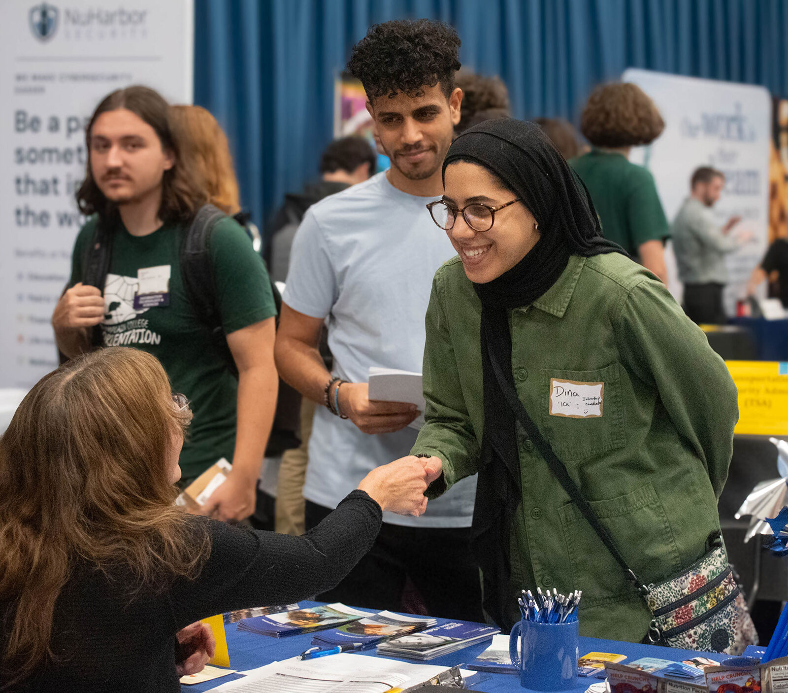 A student shakes hands with an employer across a table at the Career Fair