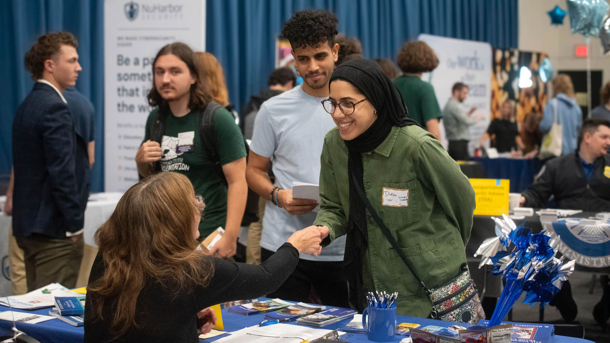 A student shakes hands with an employer across a table at the Career Fair