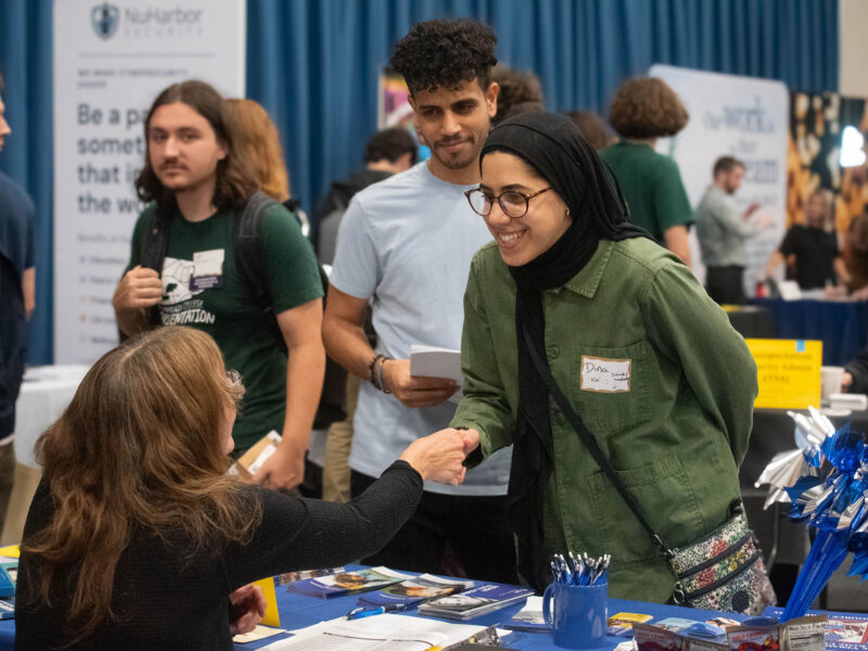 A student shakes hands with an employer across a table at the Career Fair