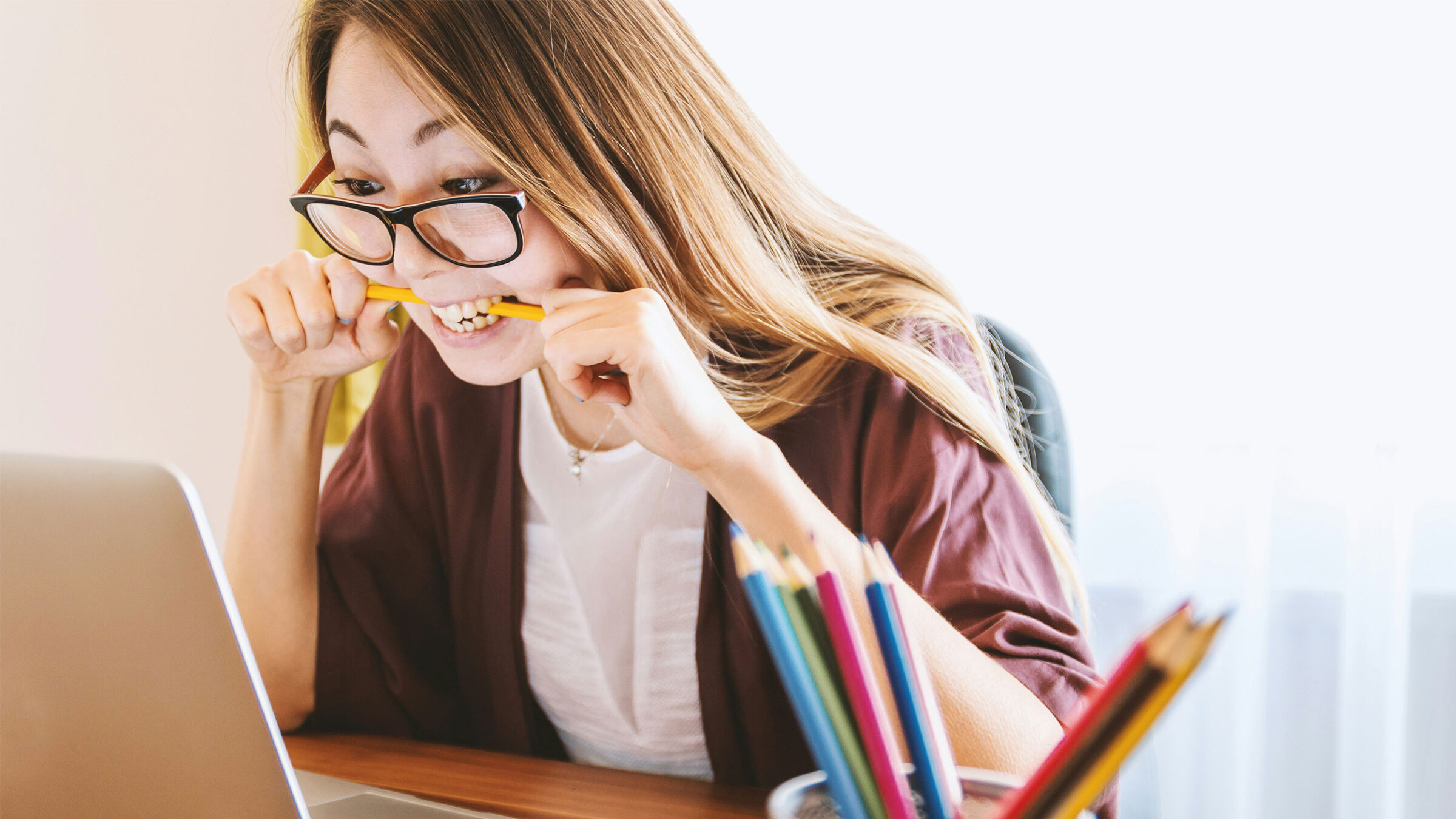 student biting a pencil while sitting at a laptop