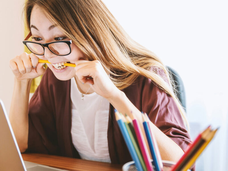 student biting a pencil while sitting at a laptop