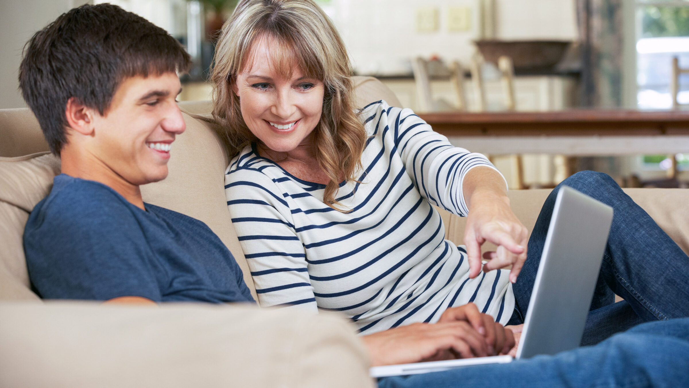 Mother With Teenage Son Sitting On Sofa At Home Using Laptop