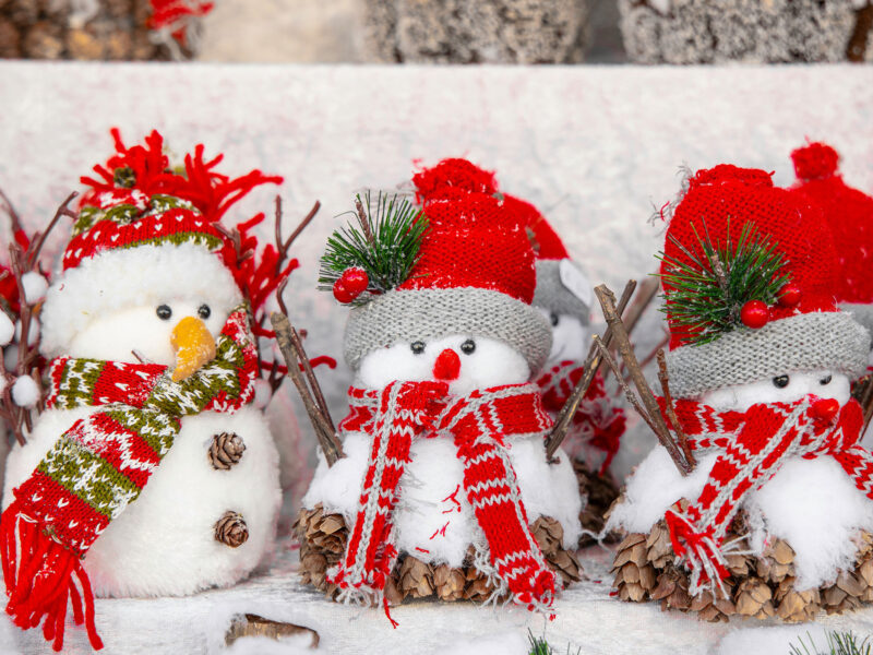 three small stuffed animal snowmen dressed in red winter hats and scarves