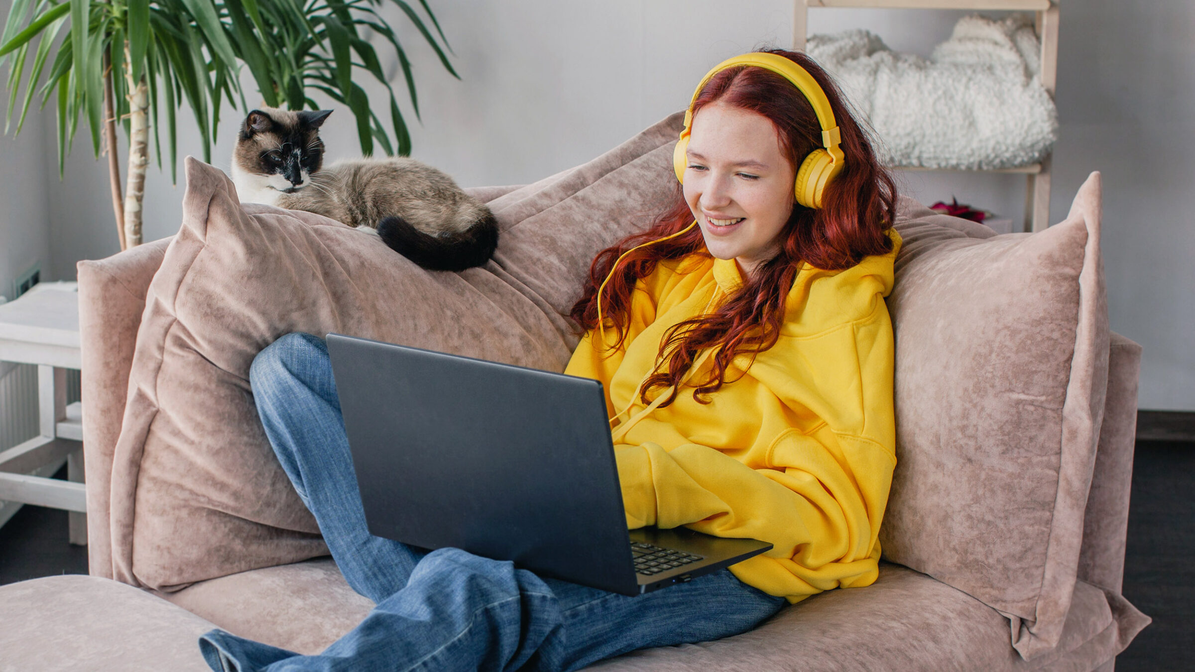 Smiling young Caucasian woman sit on couch in living room typing working on laptop, happy millennial teen girl browsing wireless internet, texting messaging on computer at home