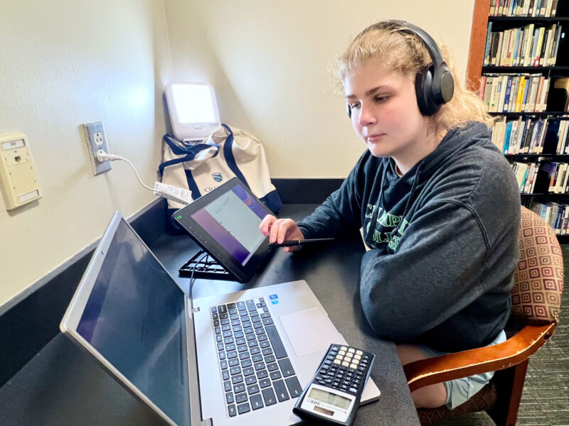 student sits at desk with laptop and a happy light