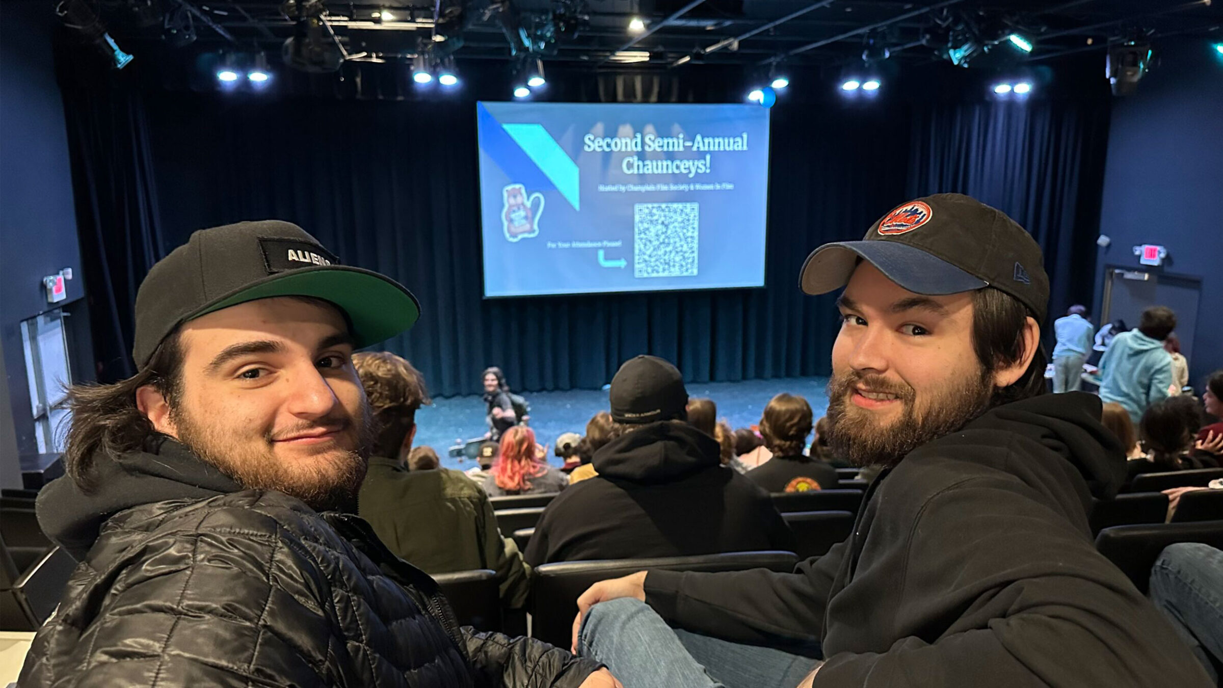 two students sitting in stadium auditorium seating at champlain, smiling over their shoulders at the camera