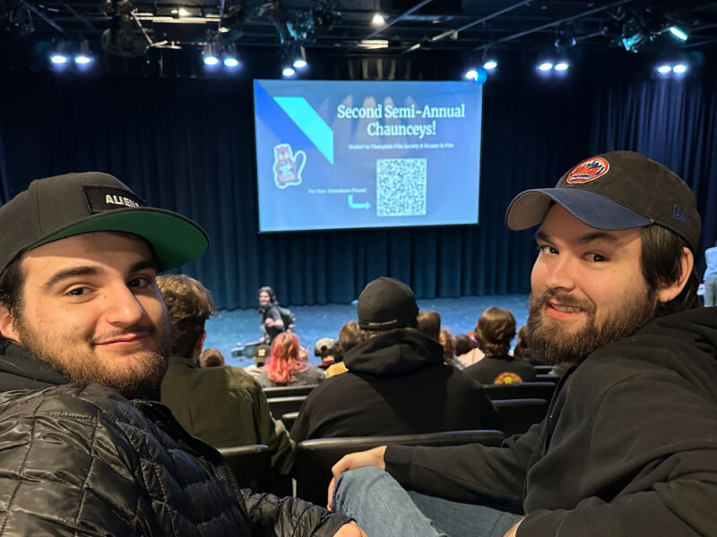 two students sitting in stadium auditorium seating at champlain, smiling over their shoulders at the camera