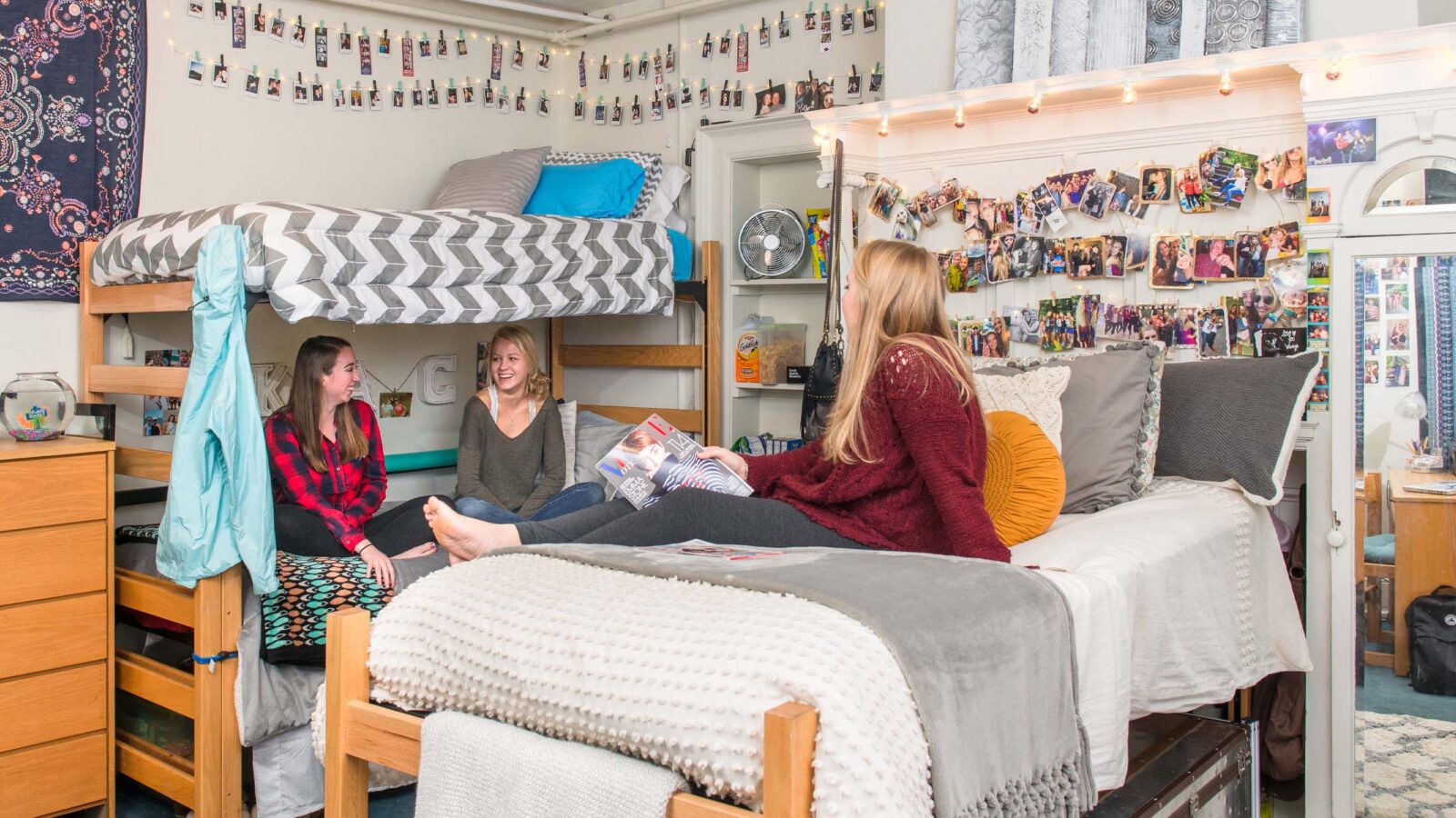 Students hanging out in a decorated dorm room. Photos and lights hang around the room