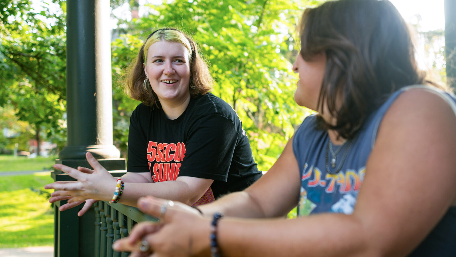 two students talk while standing on the front porch of a residence hall