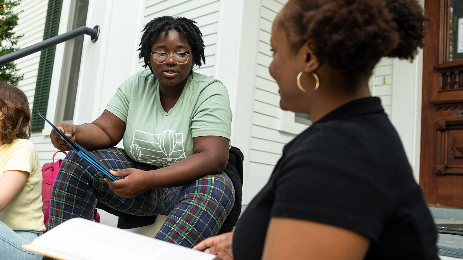 students sit on the stoop of a residence hall talking and studying