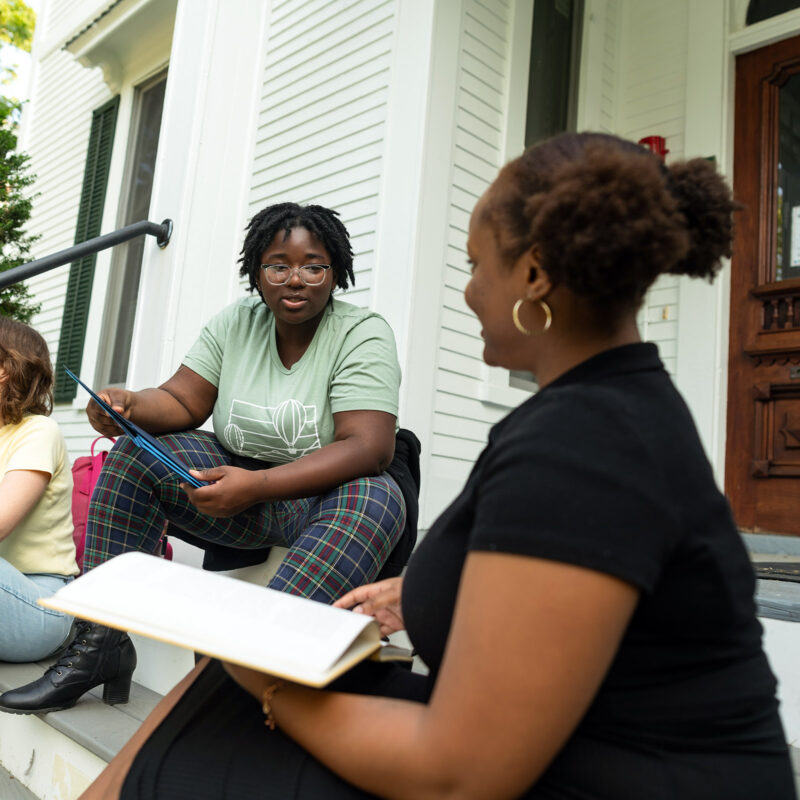 students sit on the stoop of a residence hall talking and studying