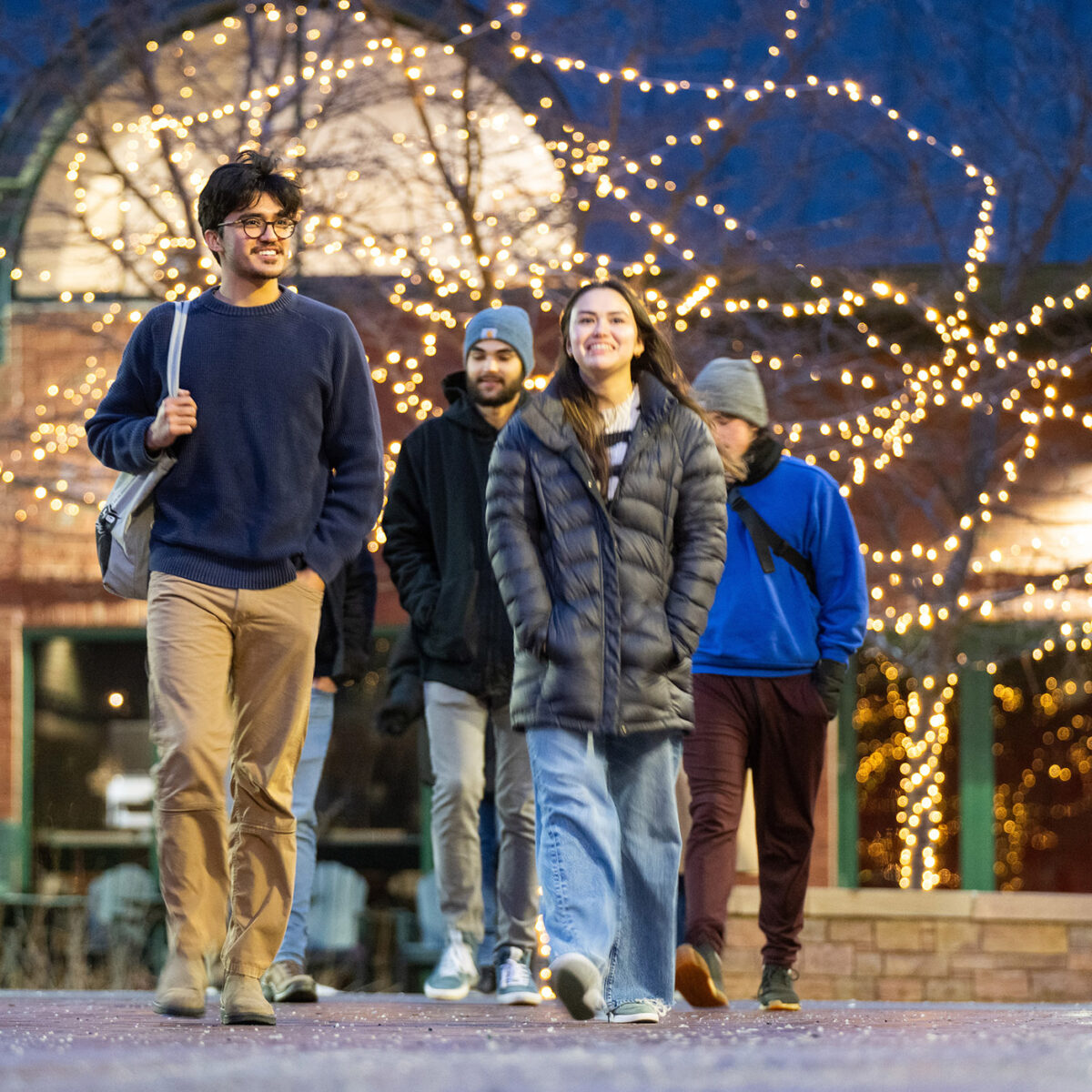 Students walking on campus under Christmas lights in the winter