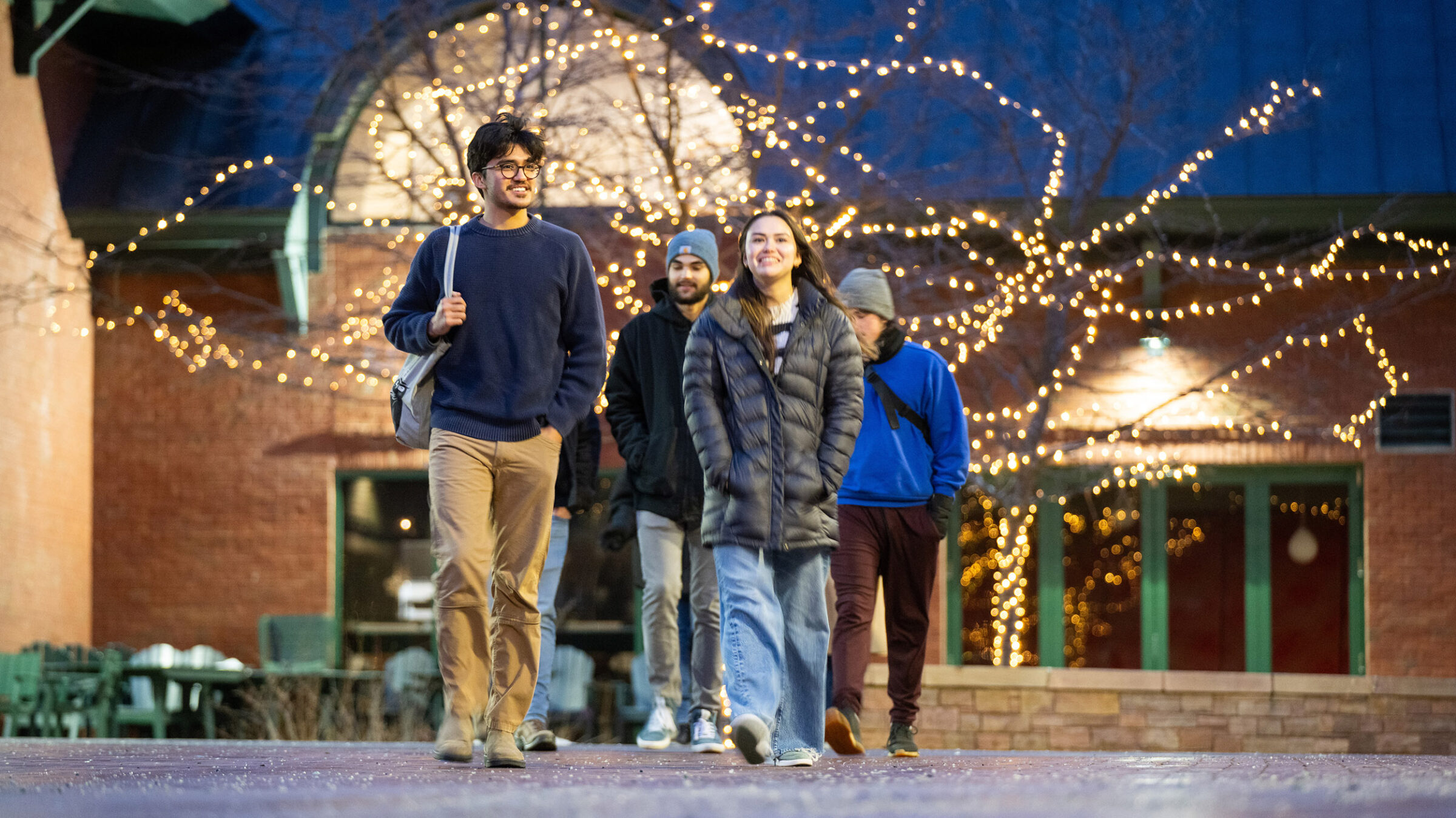 Students walking on campus under Christmas lights in the winter