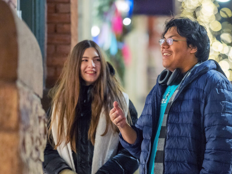 Two students having a conversation in the winter on church street under Christmas lights