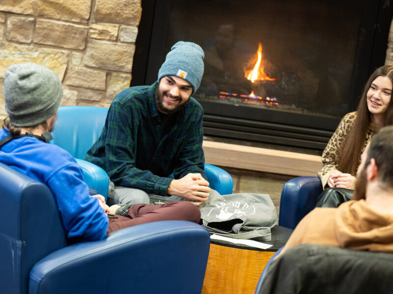 Students sitting in front of a fireplace having a conversation.