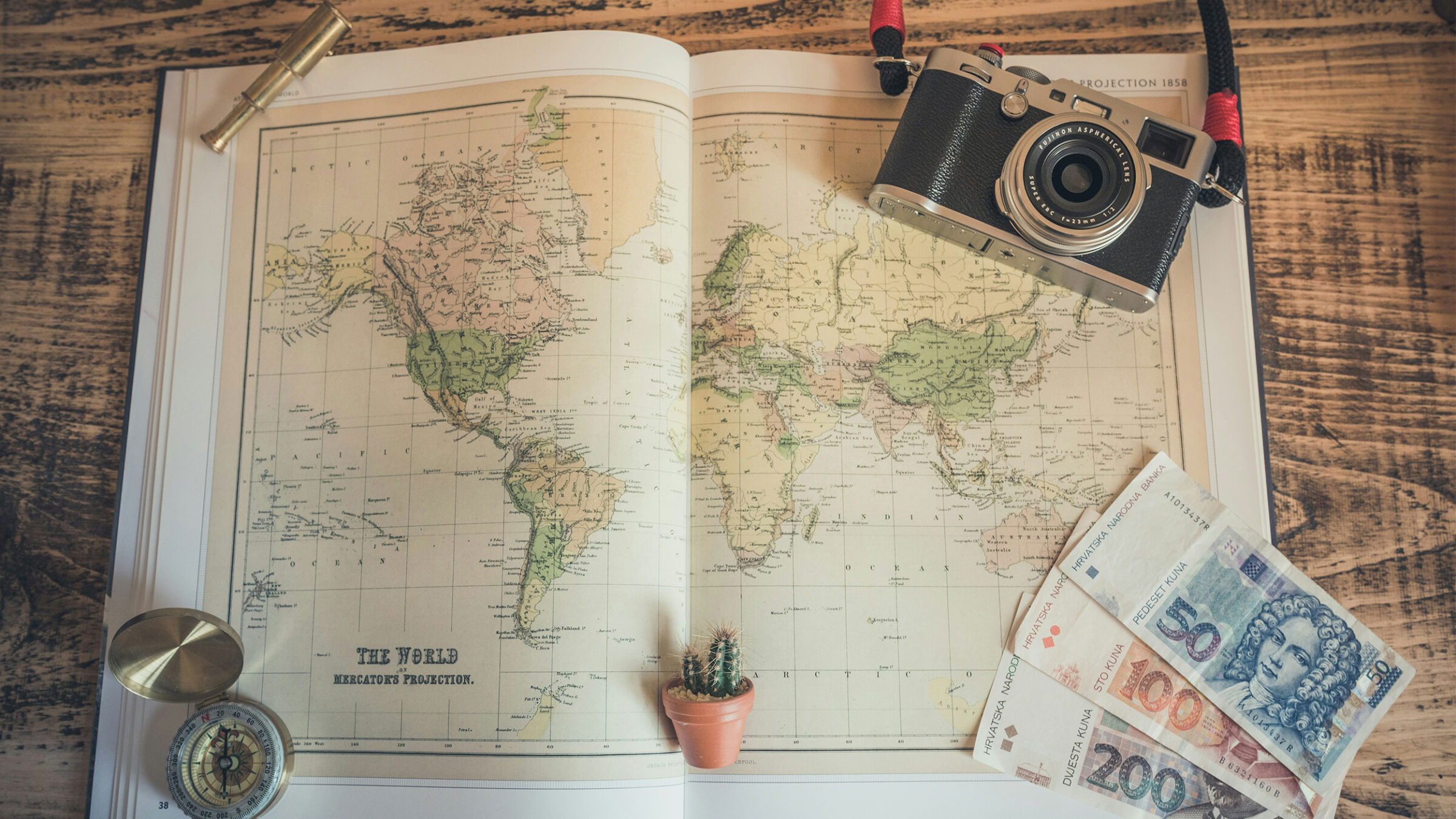 an atlas with a compass, film camera, and money featured alongside the map