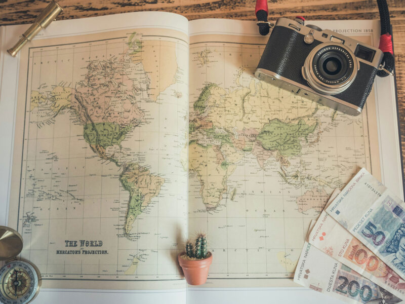 an atlas with a compass, film camera, and money featured alongside the map