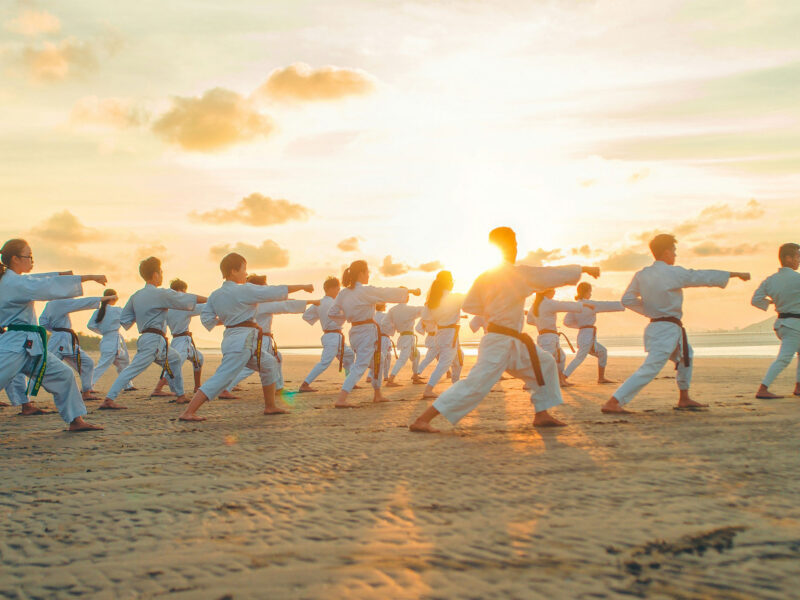 large group of people doing martial arts on the beach at sunset